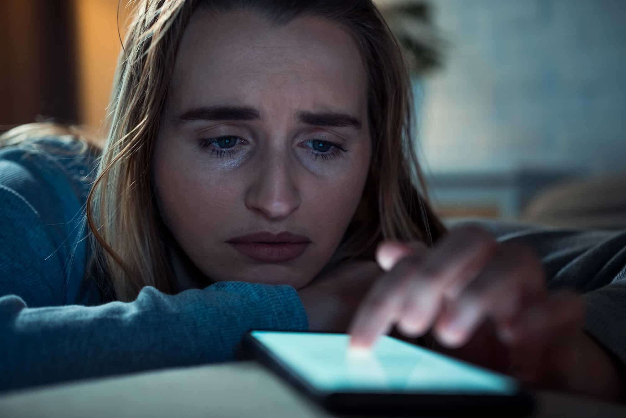 Sad woman with smart phone in living room. Depression concept.