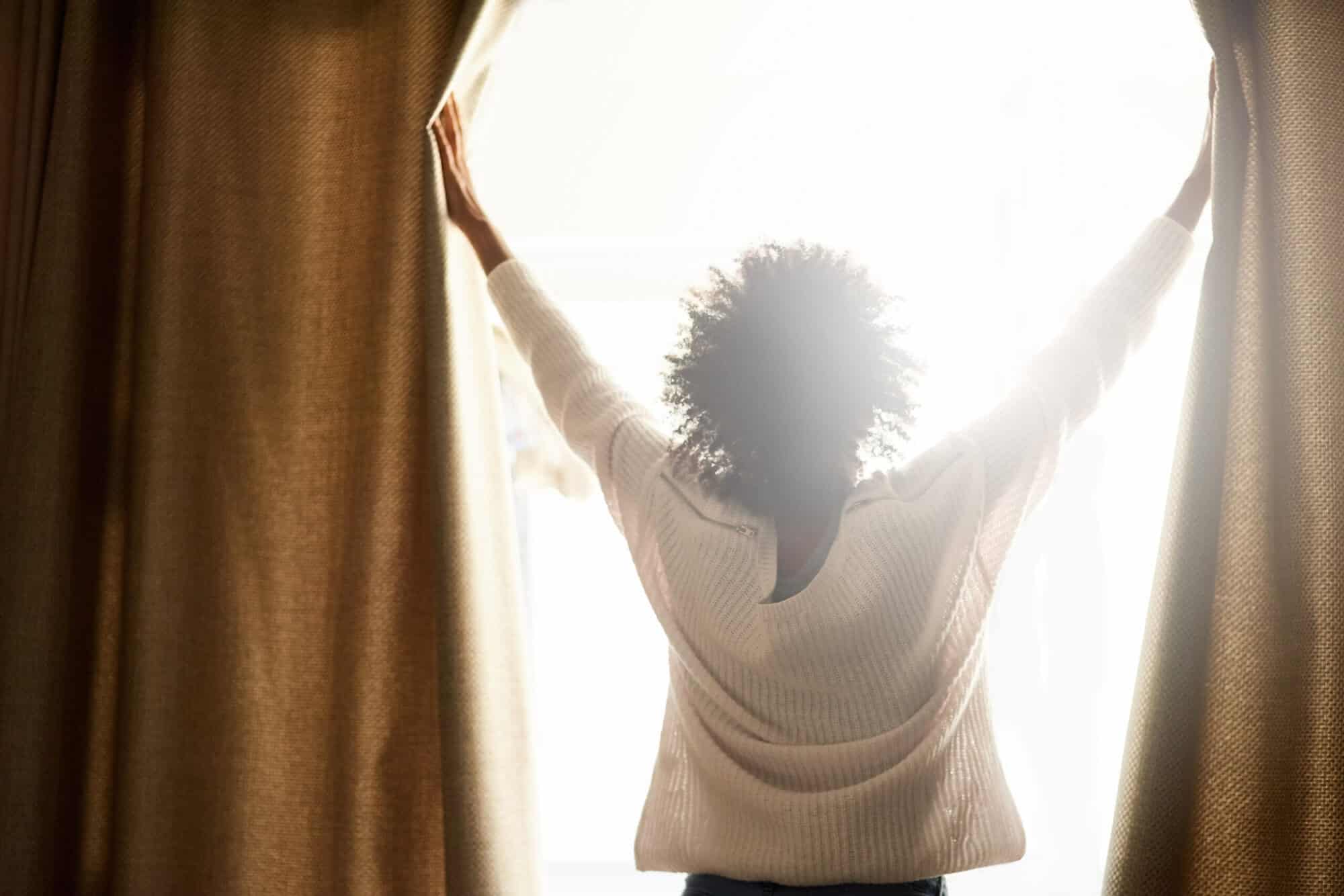 shot of a woman opening the curtains on a bright sunny day