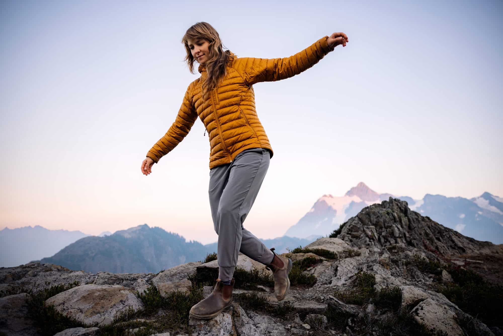 A Caucasian woman enjoys a hike on a beautiful Autumn day in Mount Baker area, Washington state, USA. She walks along. a ridge line, watching the setting sun and view of Mount Shuksan. Healthy and enjoyable lifestyle.