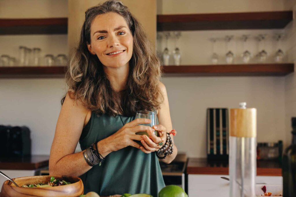 Vegan senior woman smiling while holding a glass of green juice